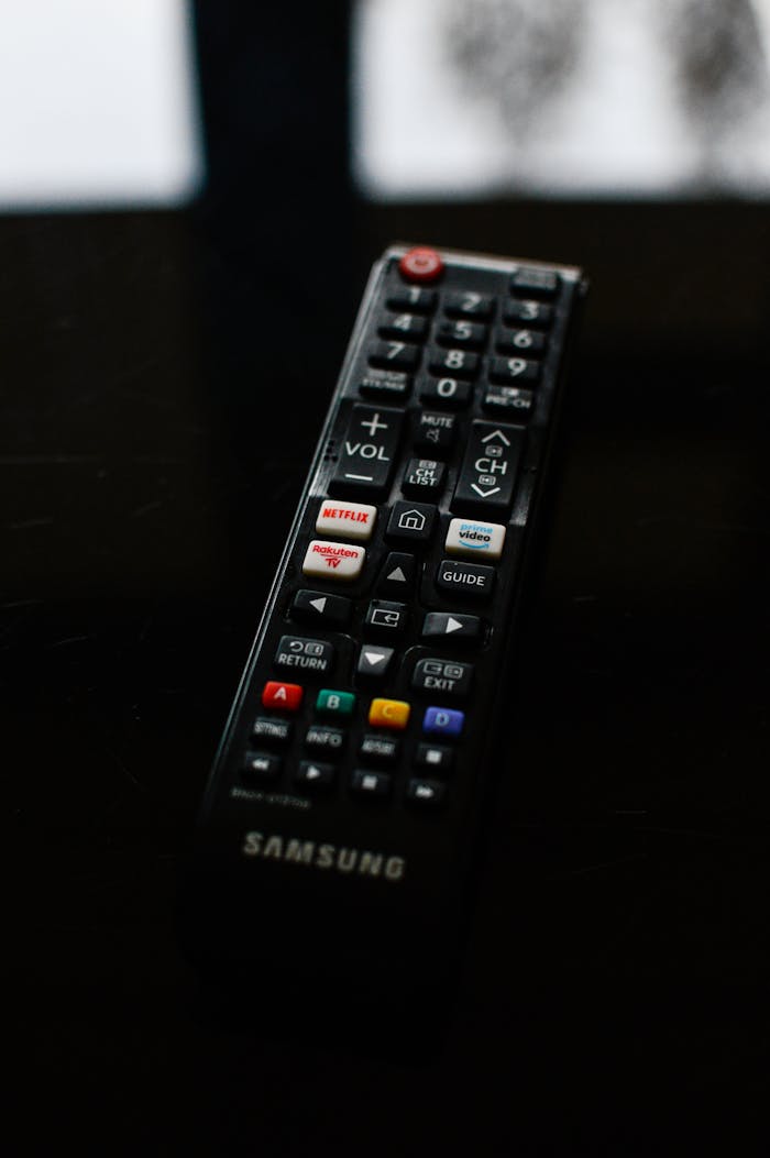 Home A detailed close-up of a Samsung TV remote resting on a dark surface, emphasizing its buttons and design.