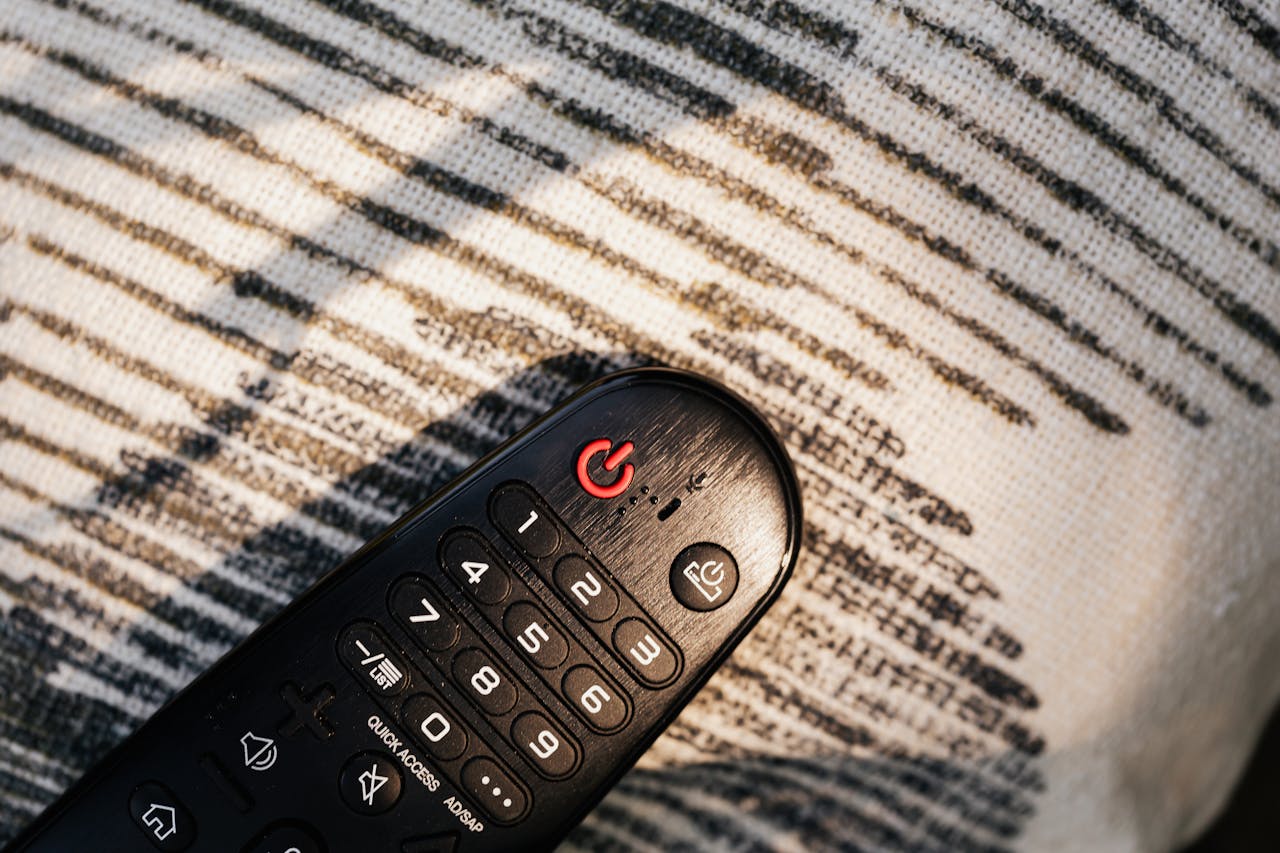 Home Close-up of a remote control on a textured knitted fabric with light shadows.